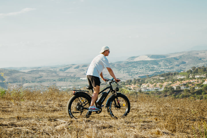 Man is riding a black kingbull electric bicycle while standing on a hill of rugged meadow