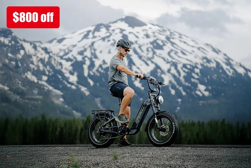 Cyclist riding black Kingbull Jumper Go electric bike with snow-capped mountains in background and $800 off promotional banner