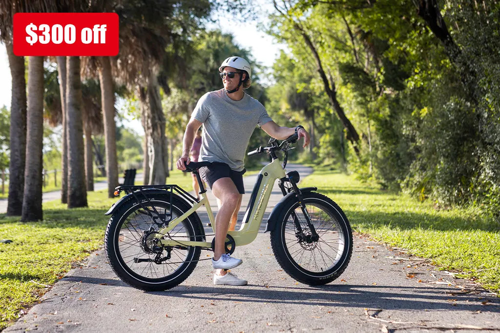 Male cyclist riding beige Kingbull Trekker electric bike on park pathway wearing helmet and sunglasses with tree-lined surroundings and $300 off promotional banner