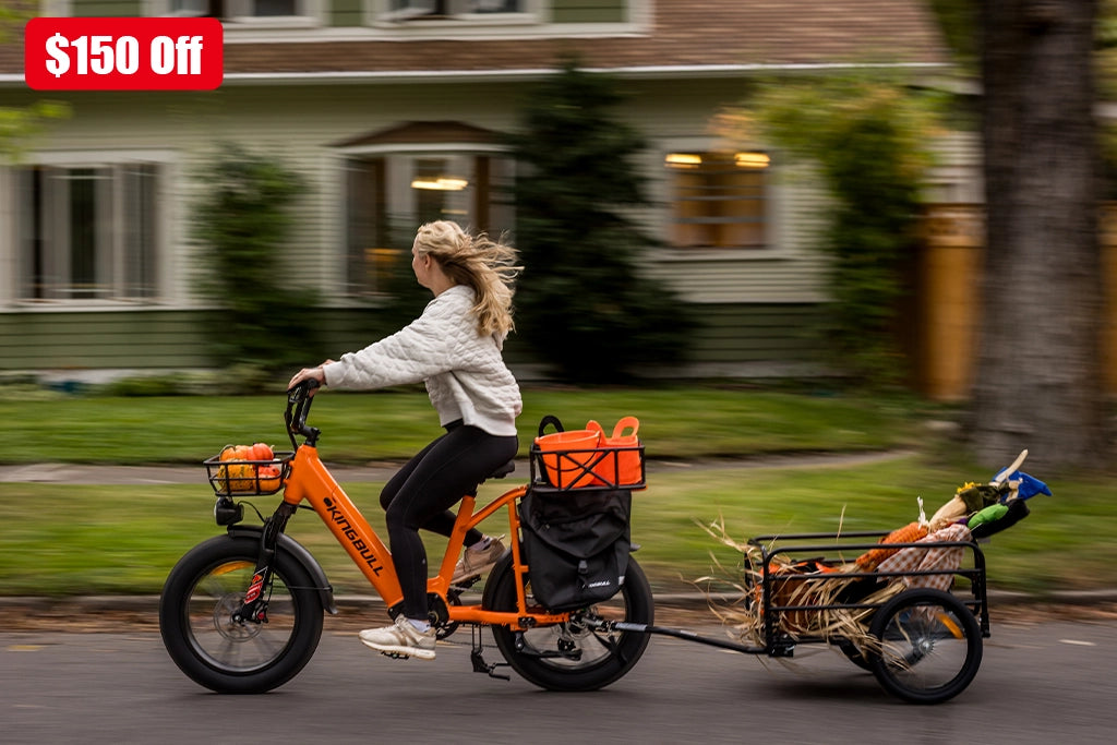 Woman riding orange Kingbull Voyager 2.0 electric bike with child trailer through residential neighborhood - $150 off promotion