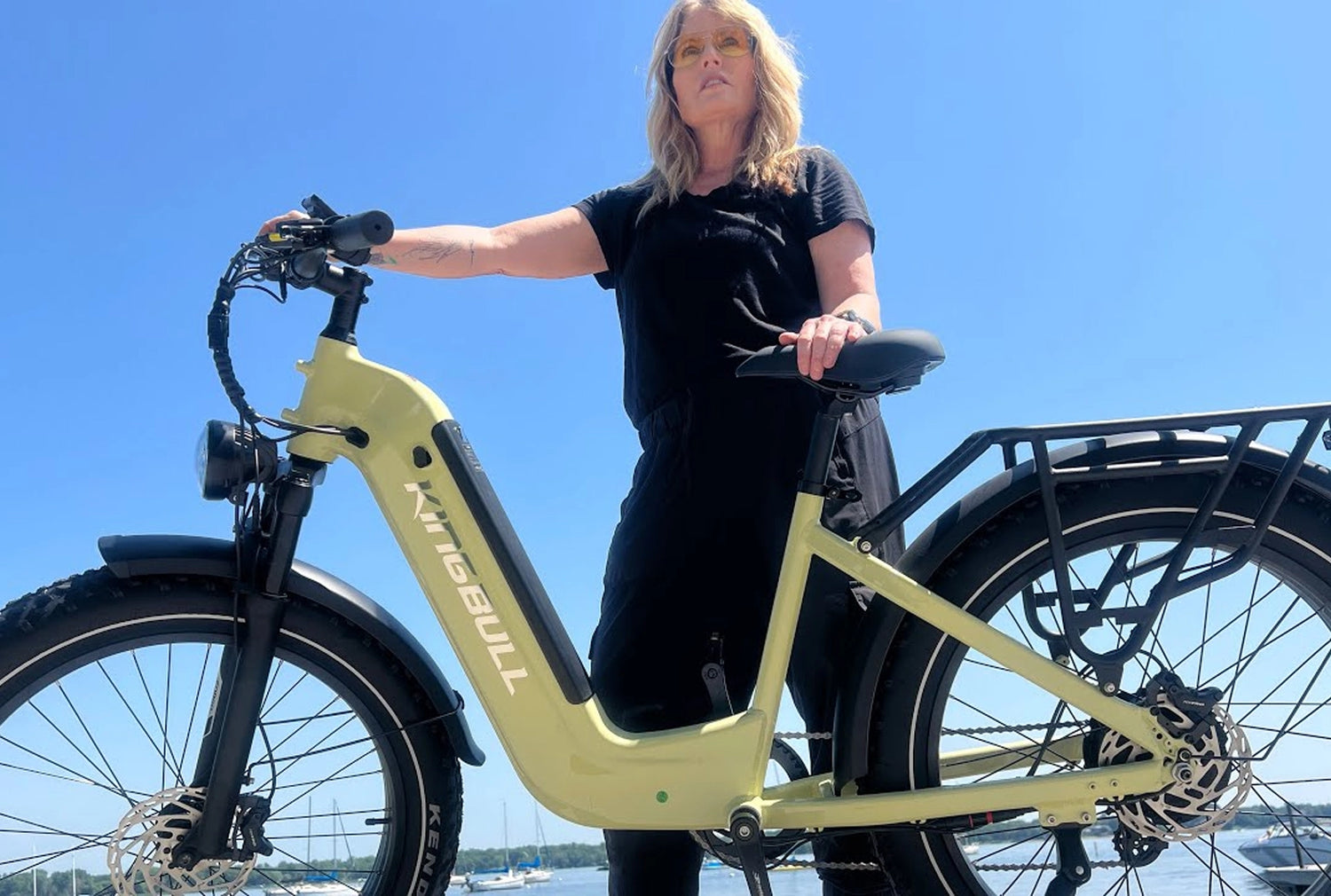 Light green KINGBULL e - bike showcased by a woman in black by the water, with clear blue sky in the background