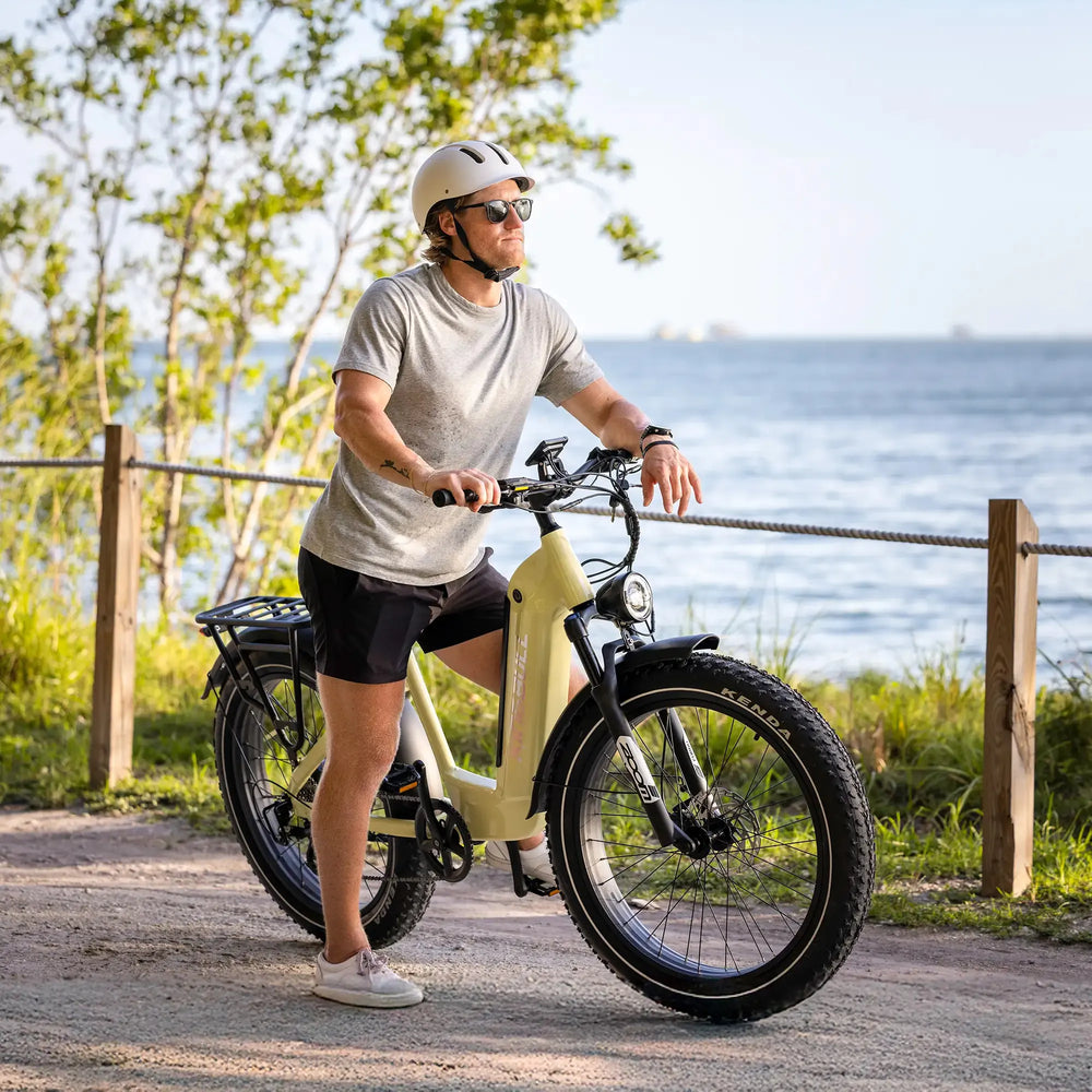 Man in helmet riding a green Kingbull Trekker low-step ebike with fat tires and a rear rack on a coastal path.