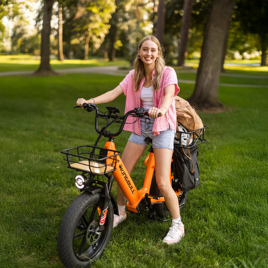 Smiling woman posing with orange Kingbull Voyager 2.0 electric bike in park setting