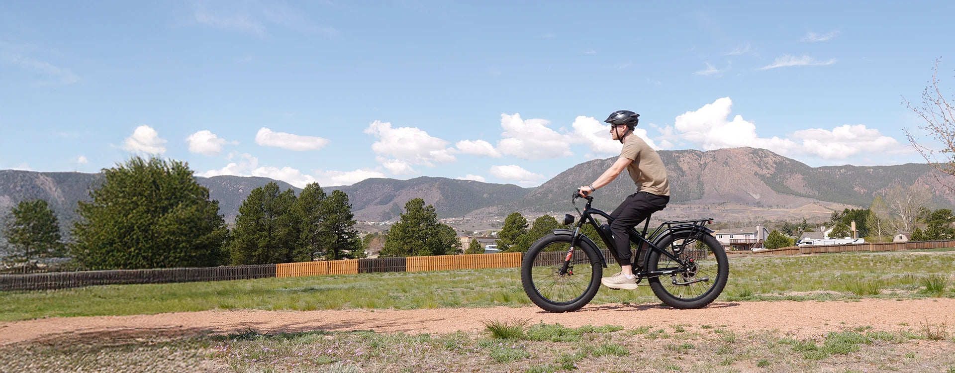 Man wearing helmet riding black Kingbull Hunter 2.0 electric fat tire bike on rural path with mountains in background